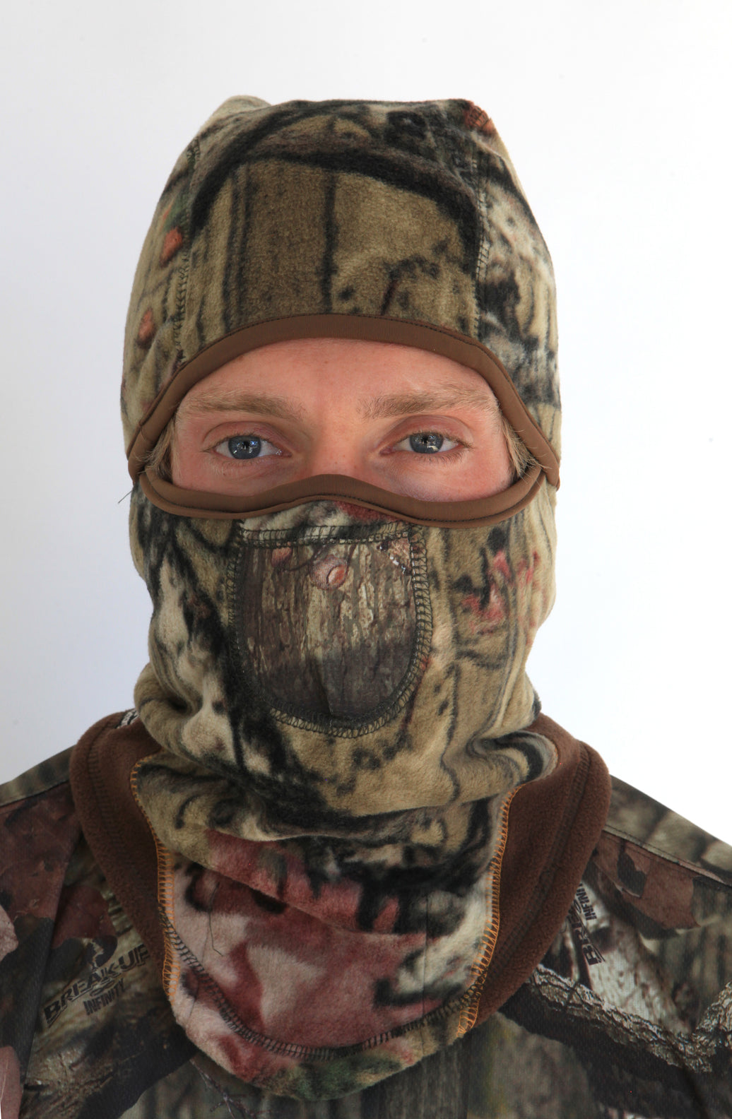 Person wearing a full-face camouflage balaclava with pockets for disposable air-activated warmers on a white background