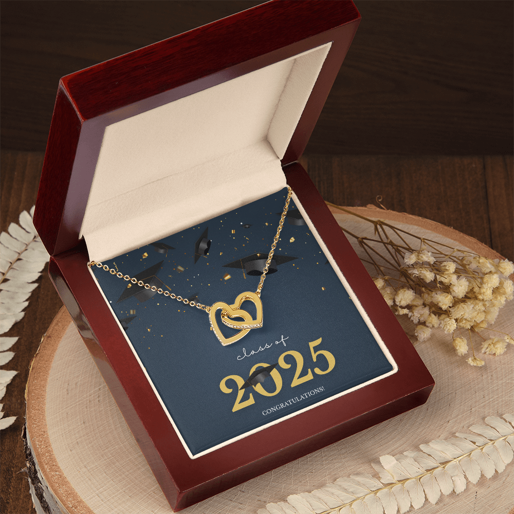 A gold interlocking hearts necklace displayed in a cherry wood box with a message card that reads "Class of 2025 – Congratulations" featuring graduation caps and celebratory confetti.