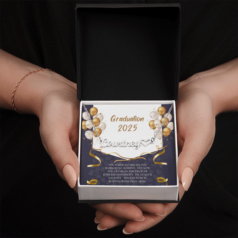 Close-up of hands holding an open red gift box featuring a personalized silver name necklace with heart, set against a message card that reads "Graduation 2025" and includes an inspiring graduation quote, with gold and white balloons in the background.