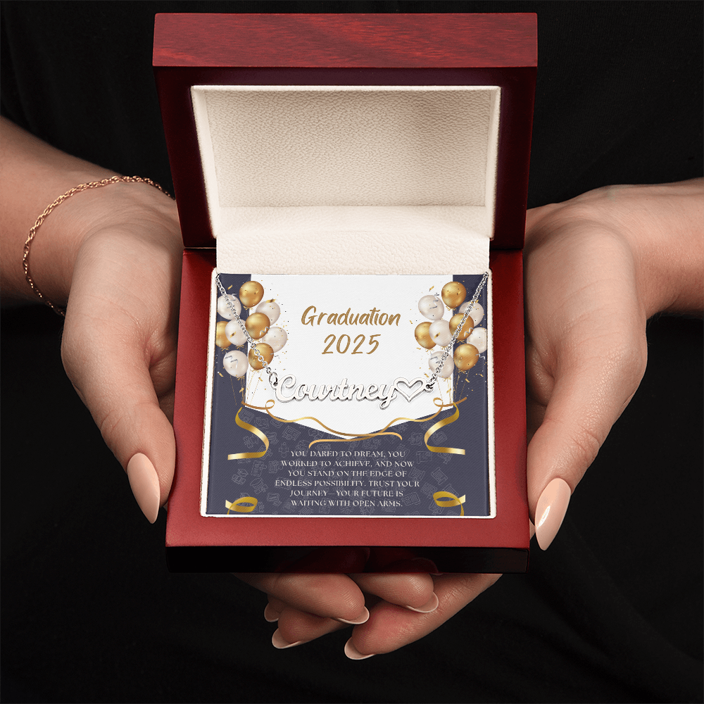 Close-up of hands holding an open red gift box featuring a personalized silver name necklace with heart, set against a message card that reads "Graduation 2025" and includes an inspiring graduation quote, with gold and white balloons in the background.