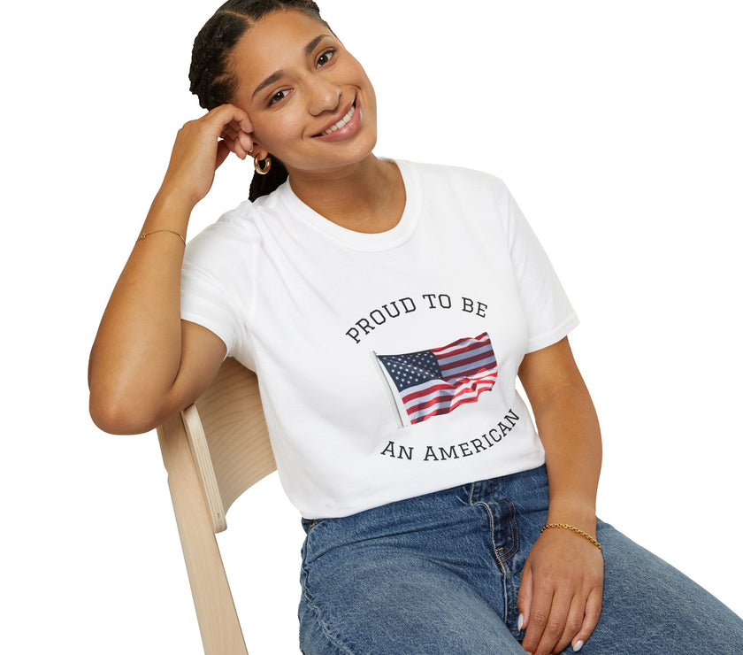 Smiling woman seated on a wooden chair wearing a white t-shirt with an American flag graphic and the words 'Proud to Be an American' printed around the flag