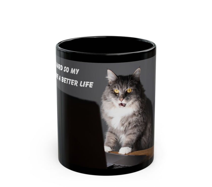 Black ceramic mug featuring a cartoon-style image of a cat sitting at a computer with the funny quote “I work hard so my cat can have a better life.”