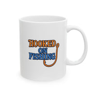 A white ceramic coffee mug displayed against a plain background, featuring the phrase "Hooked on Fishing" in bold orange and blue text with a graphic of a fishing hook integrated into the design.
