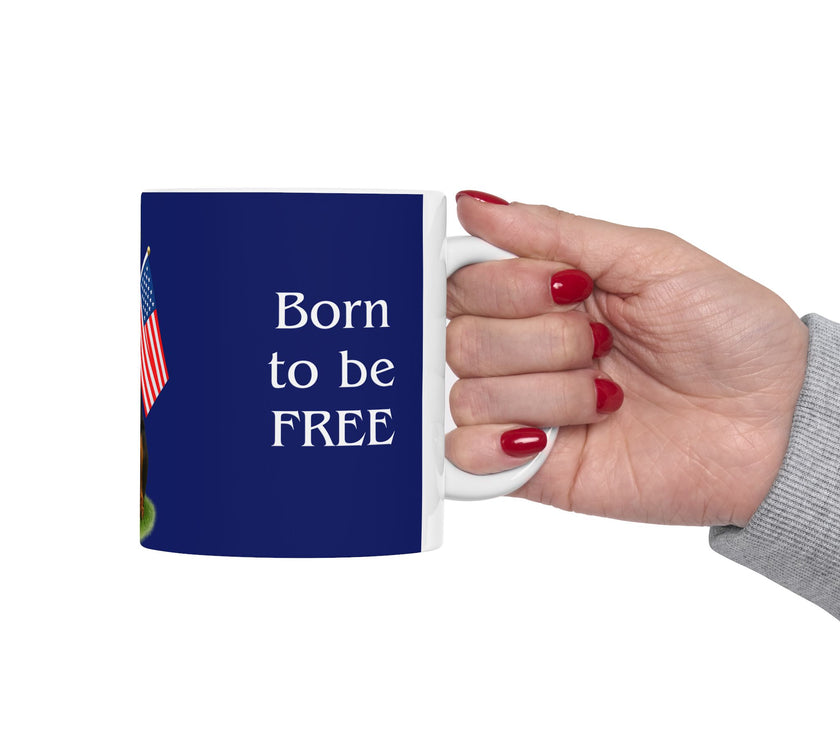 A ceramic mug featuring a Rottweiler sitting on grass, wearing a red, white, and blue bow tie, and holding an American flag against a dark blue background. with the message "Born to be Free"
