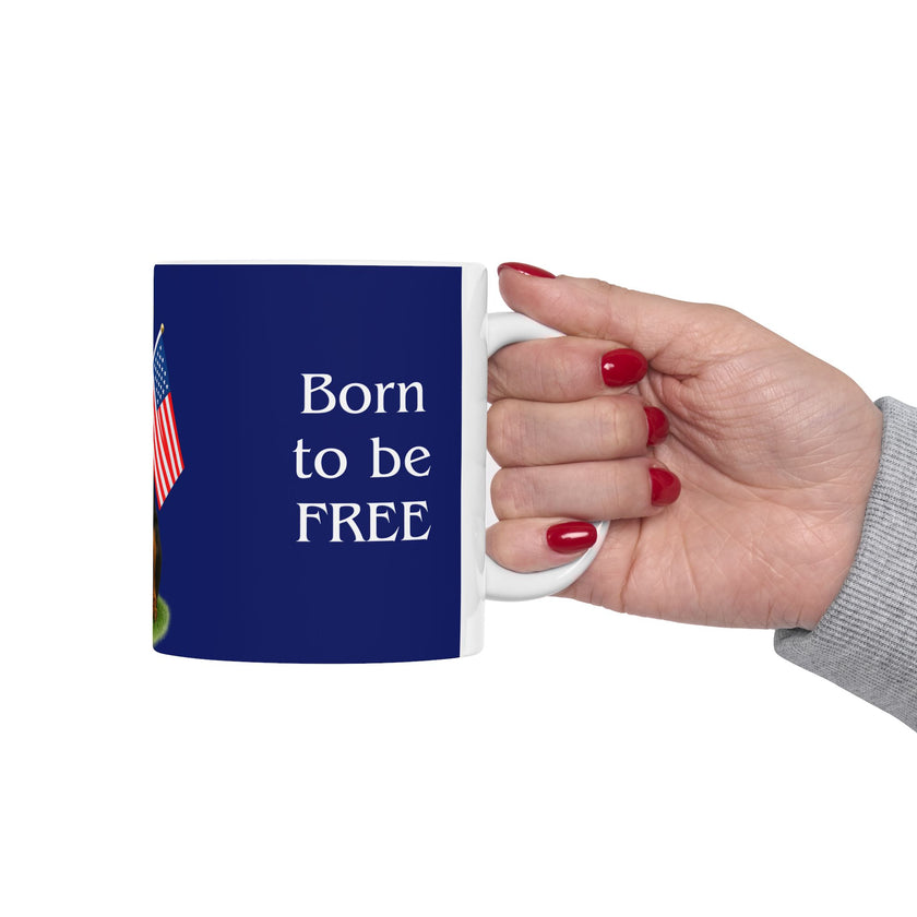 A ceramic mug featuring a Rottweiler sitting on grass, wearing a red, white, and blue bow tie, and holding an American flag against a dark blue background. with the message "Born to be Free"