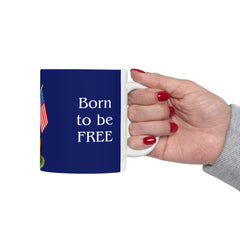 A ceramic mug featuring a Rottweiler sitting on grass, wearing a red, white, and blue bow tie, and holding an American flag against a dark blue background. with the message "Born to be Free"