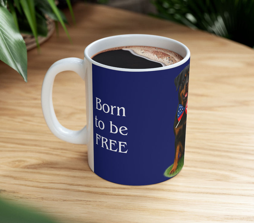 A ceramic mug featuring a Rottweiler sitting on grass, wearing a red, white, and blue bow tie, and holding an American flag against a dark blue background. with the message "Born to be Free"