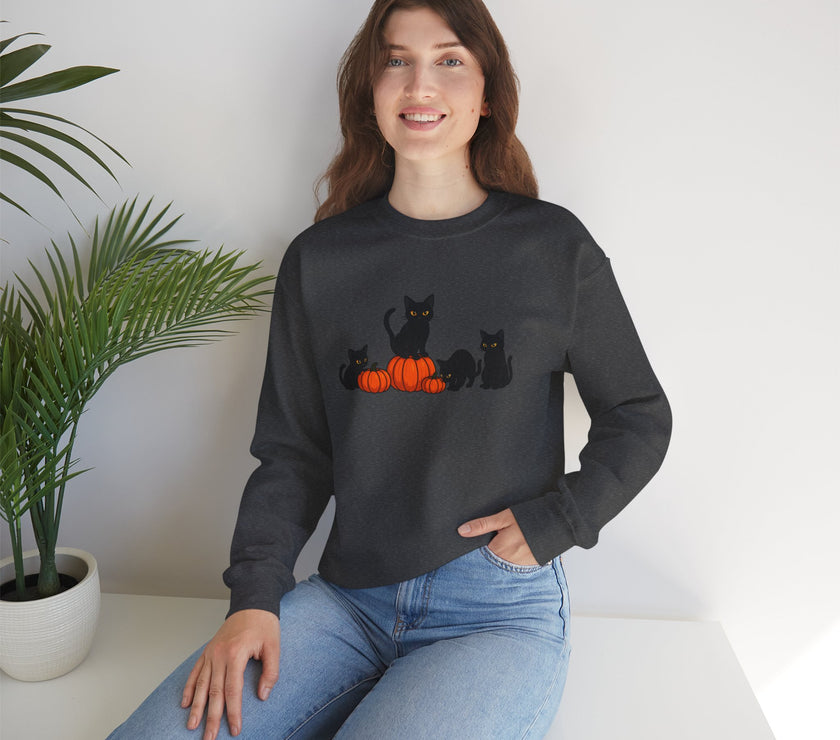 Woman wearing a black sweatshirt with cat and pumpkin design, sitting on a white surface with a plant in the background.