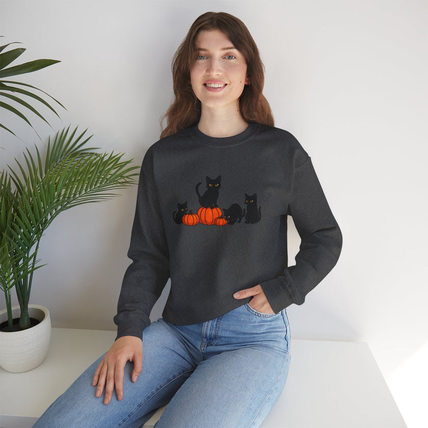 Woman wearing a black sweatshirt with cat and pumpkin design, sitting on a white surface with a plant in the background.