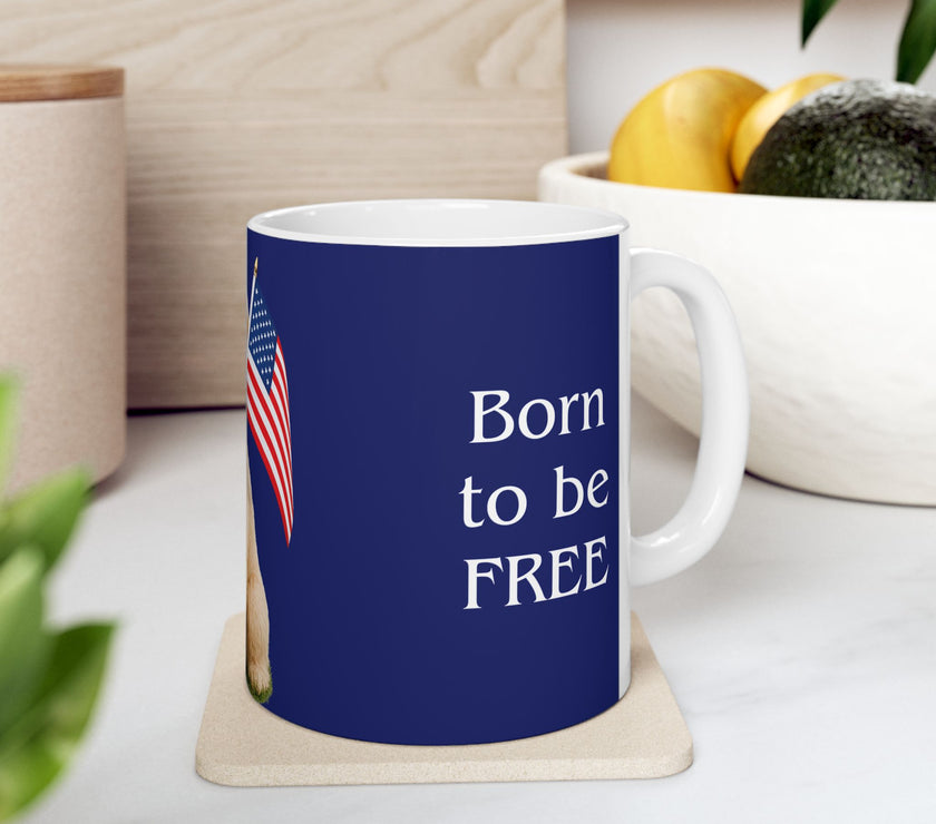 A ceramic mug featuring aGoldendoodle sitting on grass, wearing a red, white, and blue bow tie, and holding an American flag against a dark blue background. with the message "Born to be Free"  side view