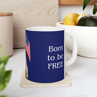 A ceramic mug featuring aGoldendoodle sitting on grass, wearing a red, white, and blue bow tie, and holding an American flag against a dark blue background. with the message "Born to be Free"  side view