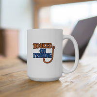 A white ceramic coffee mug displayed on a table with a laptop, featuring the phrase "Hooked on Fishing" in bold orange and blue text with a graphic of a fishing hook integrated into the design.