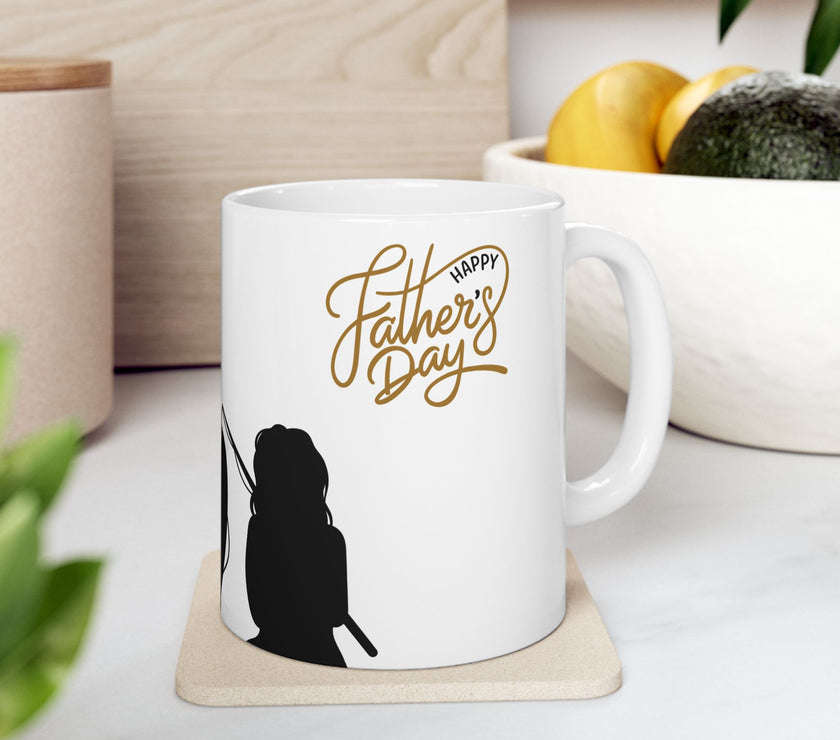 White ceramic mug featuring a silhouette of a child holding a fishing rod next to an adult figure, with the words "Happy Father's Day" in gold script above—an ideal gift for dads who love fishing and family time.