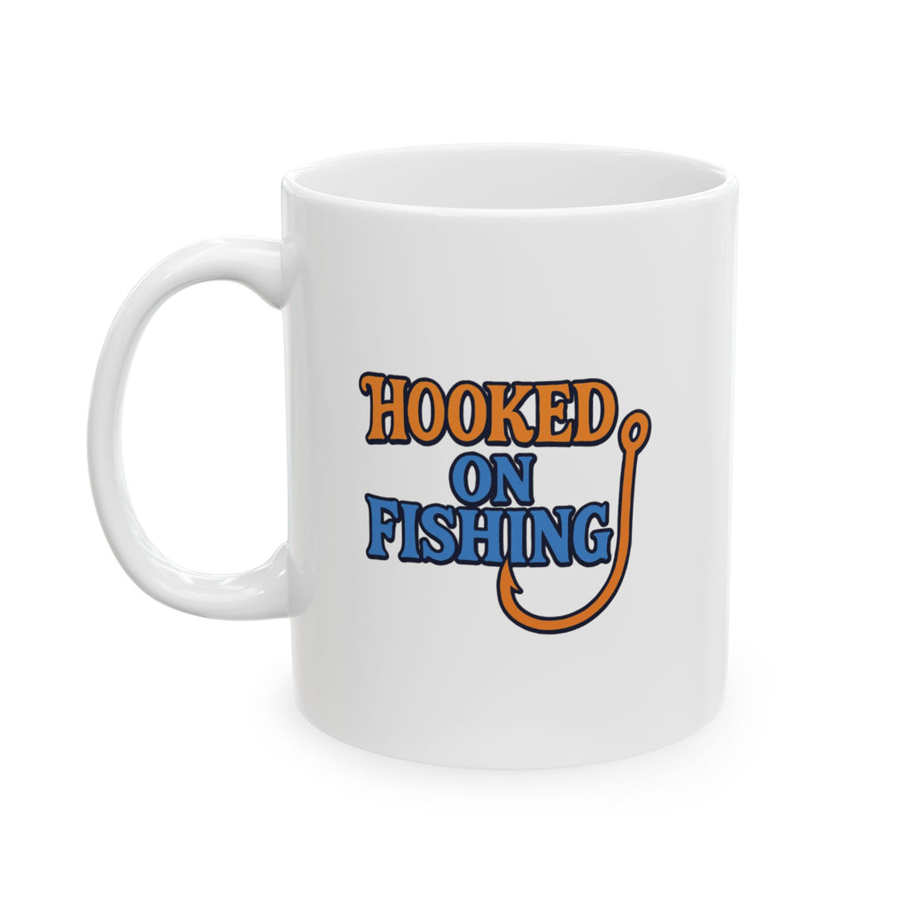 A white ceramic coffee mug displayed against a plain background, featuring the phrase "Hooked on Fishing" in bold orange and blue text with a graphic of a fishing hook integrated into the design.