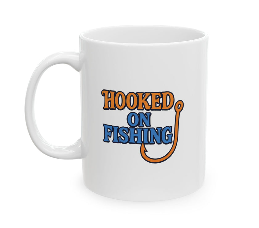 A white ceramic coffee mug displayed against a plain background, featuring the phrase "Hooked on Fishing" in bold orange and blue text with a graphic of a fishing hook integrated into the design.