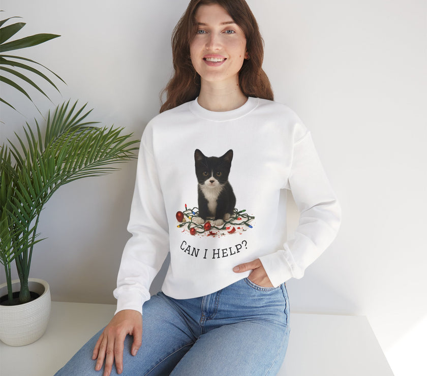 Woman wearing a white sweatshirt with a cat graphic and 'Can I Help?' text, sitting in a room with a plant.