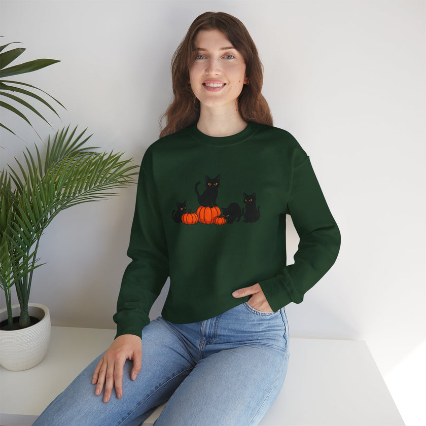 Woman wearing a green sweatshirt with black cats and pumpkins design, sitting on a white surface with a plant in the background.