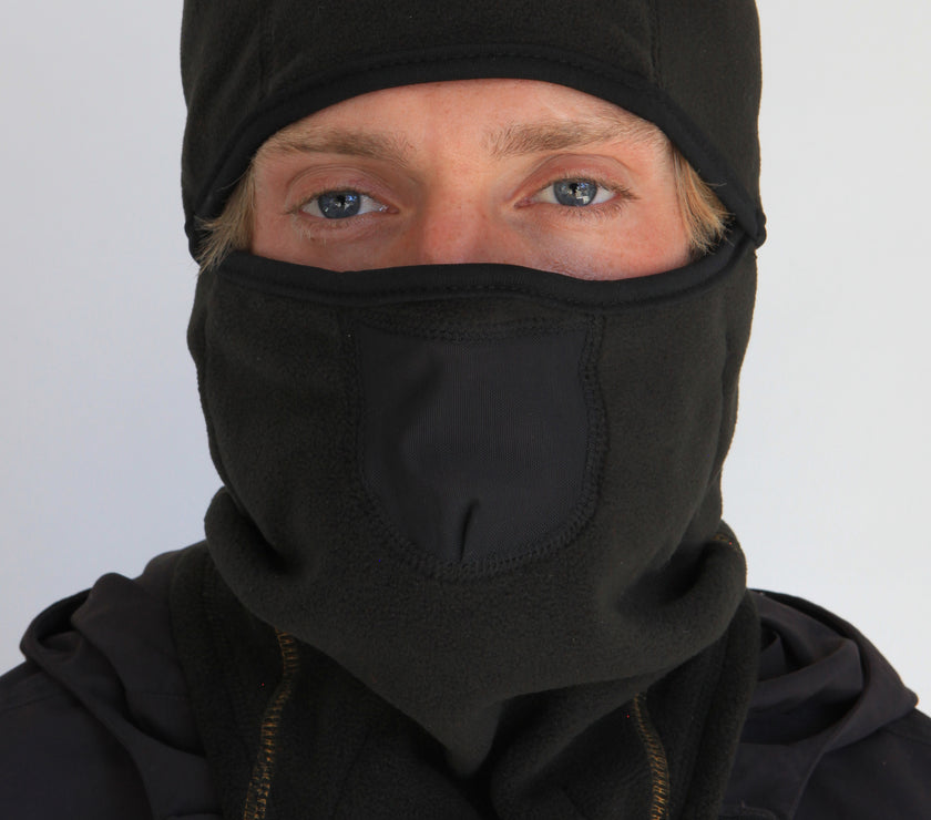 Person wearing a full-face black fleece balaclava with pockets for disposable air-activated warmers on a white background