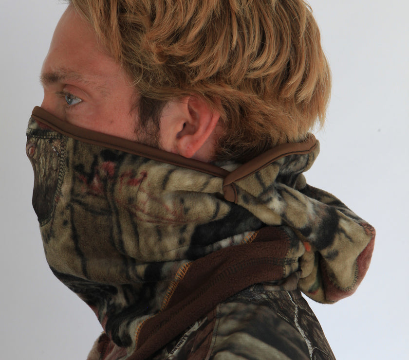 Person wearing a full-face camouflage fleece balaclava with pockets for disposable air-activated warmers on a white background