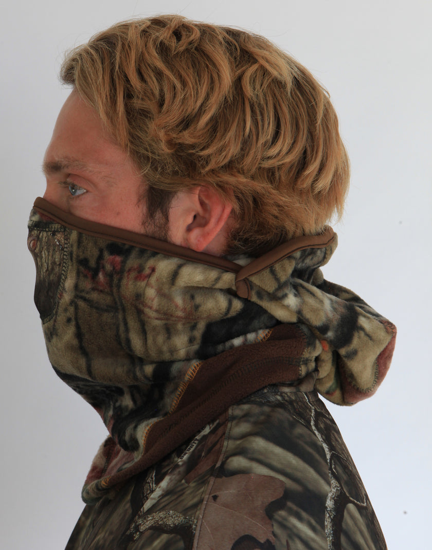Person wearing a full-face camouflage fleece balaclava with pockets for disposable air-activated warmers on a white background
