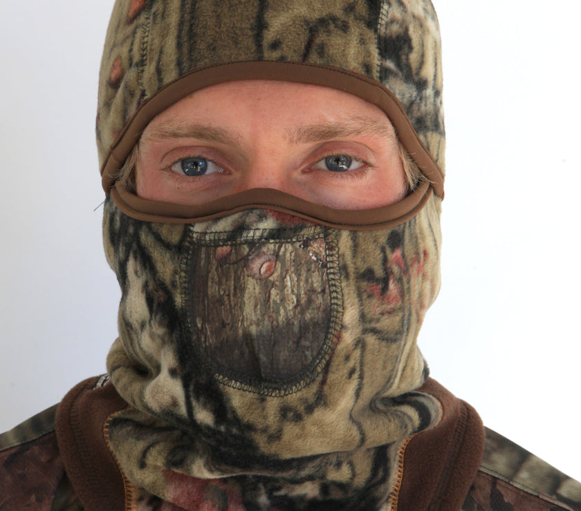 Person wearing a full-face camouflage balaclava with pockets for disposable air-activated warmers on a white background