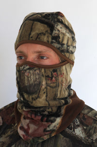 Person wearing a full-face camouflage fleece balaclava with pockets for disposable air-activated warmers on a white background