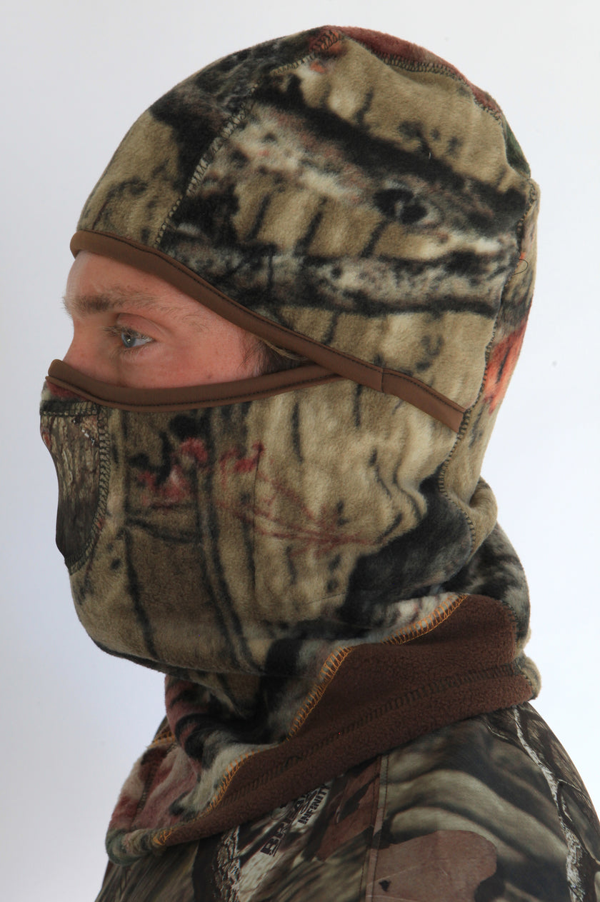 Person wearing a full-face camouflage fleece balaclava with pockets for disposable air-activated warmers on a white background