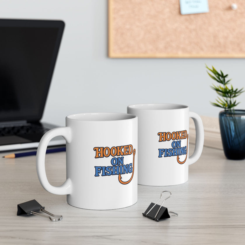 Two white ceramic coffee mug featuring the phrase "Hooked on Fishing" in bold orange and blue text with a graphic of a fishing hook integrated into the design.