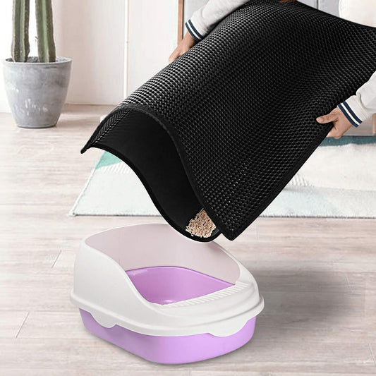 Person lifting a black mesh cover from a purple cat litter box on a wooden floor.