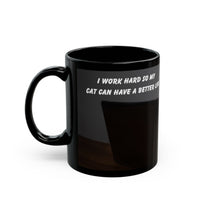 Black ceramic mug featuring a cartoon-style image of a cat sitting at a computer with the funny quote “I work hard so my cat can have a better life.”
