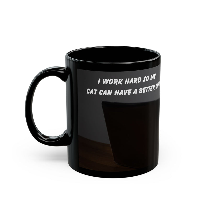 Black ceramic mug featuring a cartoon-style image of a cat sitting at a computer with the funny quote “I work hard so my cat can have a better life.”