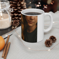 White mug with a printed design of a person's face, surrounded by decorative items like a candle, orange, and pine cones.