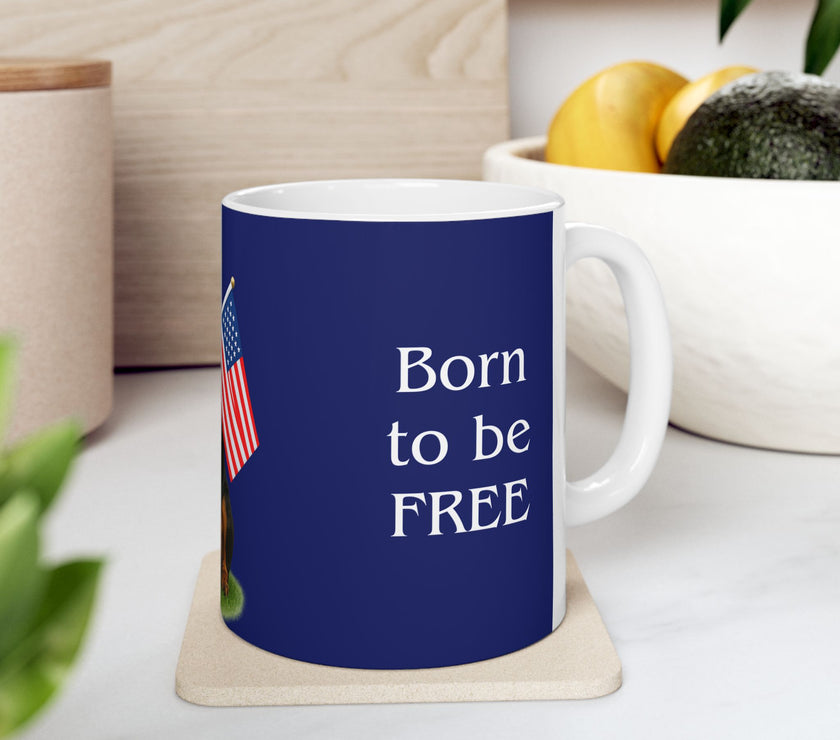 A ceramic mug featuring a Rottweiler sitting on grass, wearing a red, white, and blue bow tie, and holding an American flag against a dark blue background. with the message "Born to be Free"