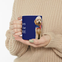 A ceramic mug featuring aGoldendoodle sitting on grass, wearing a red, white, and blue bow tie, and holding an American flag against a dark blue background. with the message "Born to be Free"