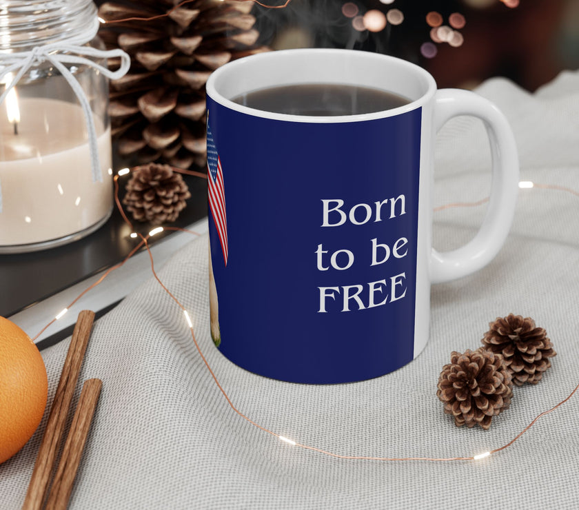 A ceramic mug featuring aGoldendoodle sitting on grass, wearing a red, white, and blue bow tie, and holding an American flag against a dark blue background. with the message "Born to be Free" side view