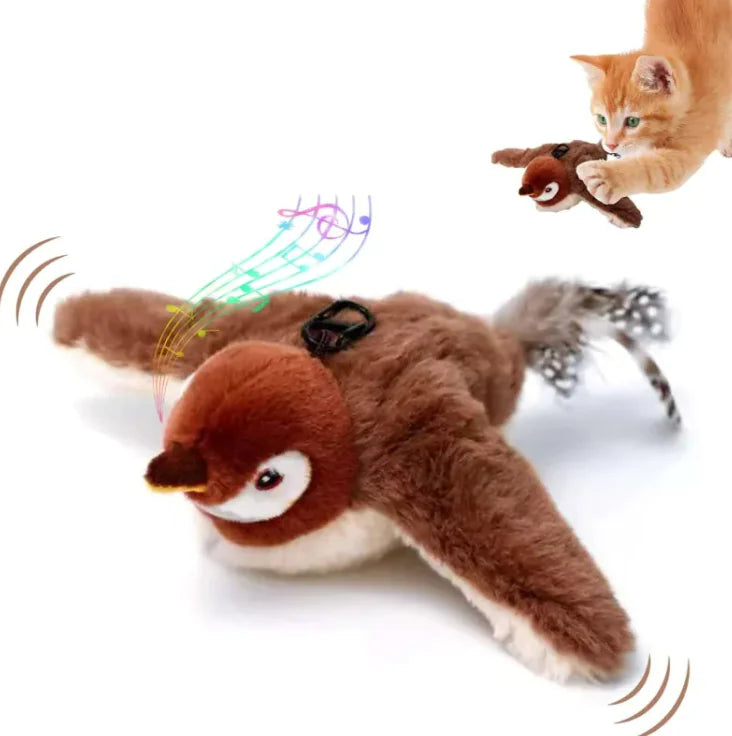 A playful orange kitten interacts with a plush brown bird cat toy that features exaggerated eyes, sound and motion effects, and colorful musical notes to indicate interactive play.