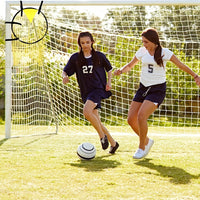 Two young girls playing soccer on a grass field with a goalpost in the background.