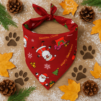 Red Christmas-themed dog bandana with Santa Claus design on a wooden surface with festive decorations.