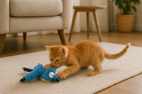 A playful orange kitten interacts with a plush blue bird cat toy that features exaggerated eyes, sound and motion effects, and colorful musical notes to indicate interactive play.