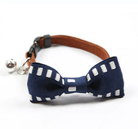 Navy blue bow tie with white polka dots on a brown leather collar with a bell, on a white background.