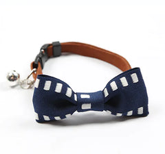 Navy blue bow tie with white polka dots on a brown leather collar with a bell, on a white background.