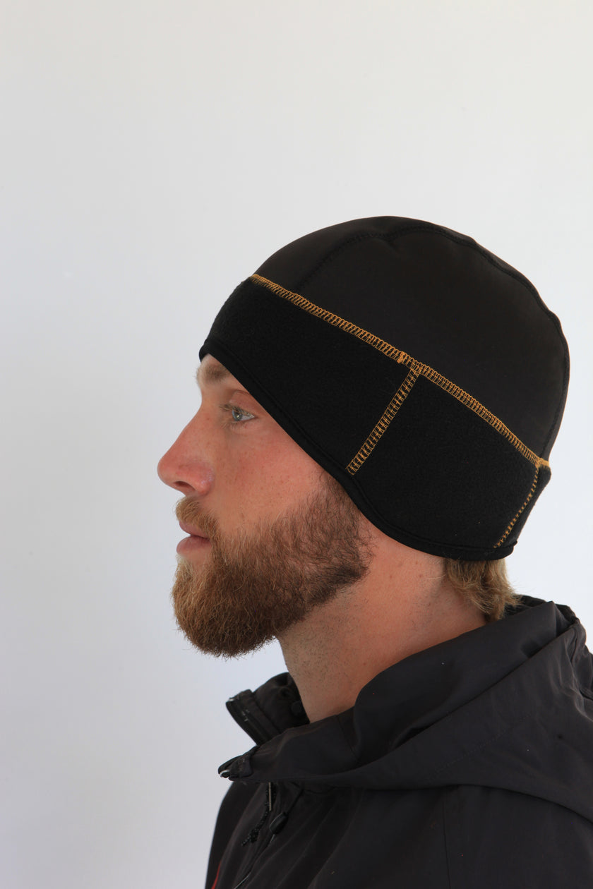 Man wearing a black beanie with gold stitching on a white background