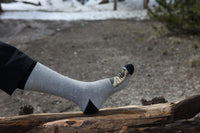 Person wearing gray socks with black toes and heels, standing on a log in a natural setting.
