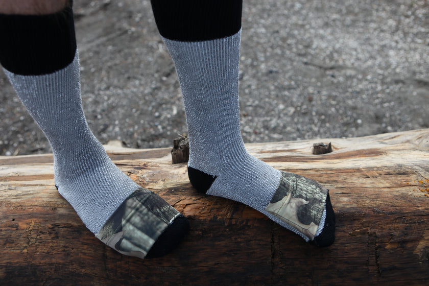 Person wearing light blue socks with camouflage toe and heel on a log.