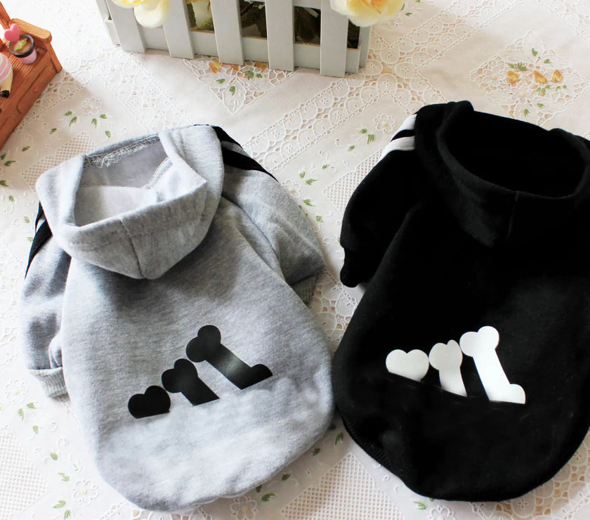 Two pet hoodies, one gray with black paw prints and one black with white paw prints, on a light surface.