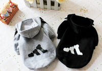 Two pet hoodies, one gray with black paw prints and one black with white paw prints, on a light surface.