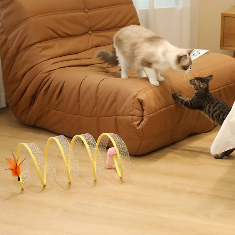 Two cats playing with a toy on a brown couch.