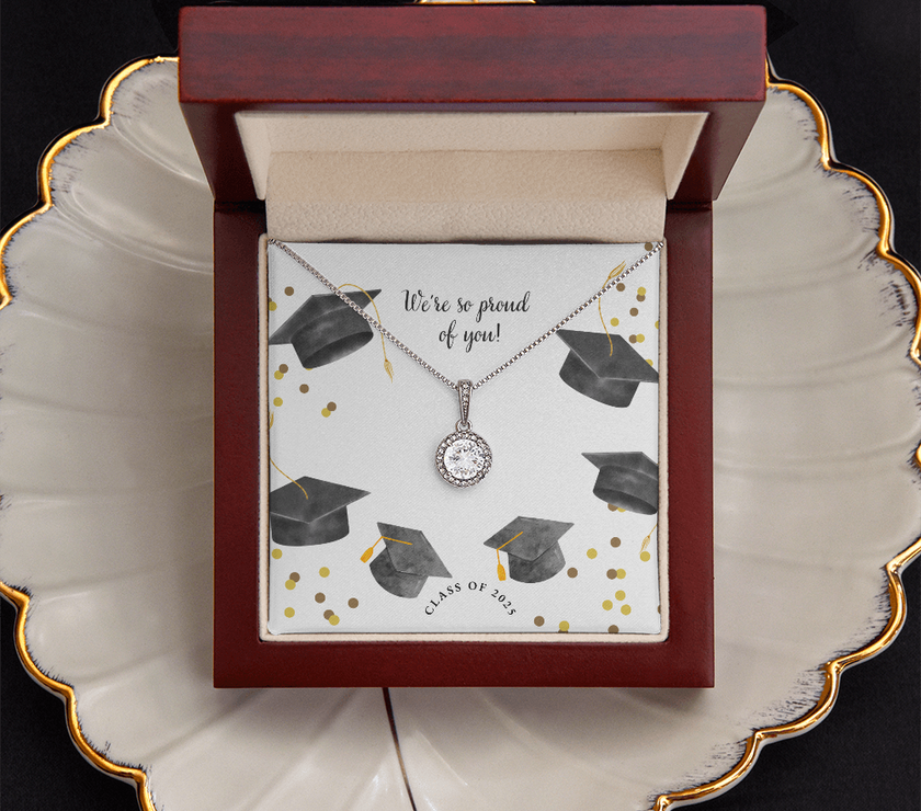 Open gift box displaying a sparkling silver Eternal Hope necklace with a round pendant, set against a graduation-themed message card that reads "We're so proud of you!" with graduation caps, gold confetti, and "Class of 2025" text.