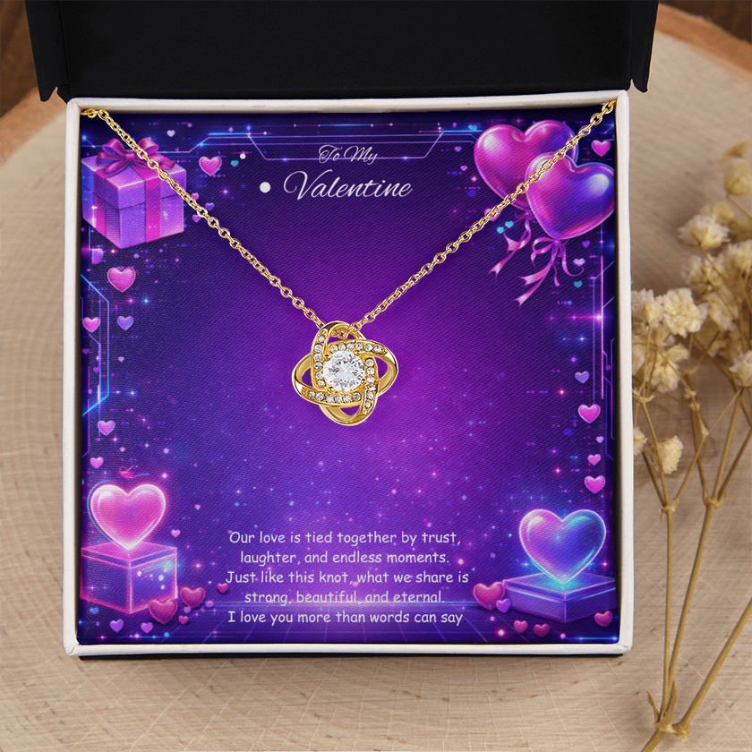 Gold love knot necklace with a sparkling center stone displayed on a purple Valentine’s Day background with glowing hearts, symbolizing eternal love and romantic connection.
