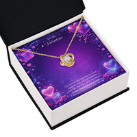 Gold love knot necklace with a sparkling center stone displayed on a purple Valentine’s Day background with glowing hearts, symbolizing eternal love and romantic connection.